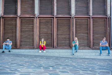 Young people wearing face safety masks using smart mobile phones while keeping social distance during coronavirus time - Technology and covid-19 spread prevention concept - Focus on faces