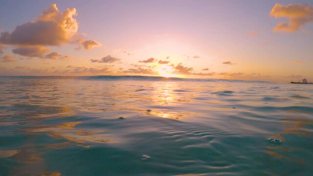 SLOW MOTION, CLOSE UP, LENS FLARE: Golden evening sunbeams shine on a refreshing turquoise colored ocean wave sweeping over the camera. Small sea waves gently roll towards the coast of Barbados.