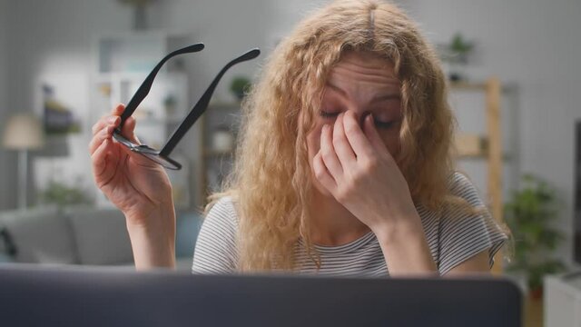 Young woman using laptop feeling discomfort from dry irritated fatigued eyes taking off glasses