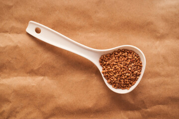 buckwheat lies in a white plastic spoon on a brown background