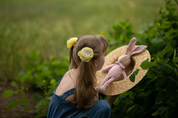 
girl with beautiful flower hairpins plays on a summer day in the garden with a rag hare in a straw hat