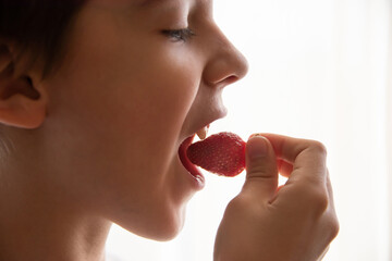 boy eating a very tasty strawberry on a light background. Close up