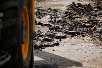 Dismantled and broken asphalt on a city street next to the wheel of a yellow construction vehicle...