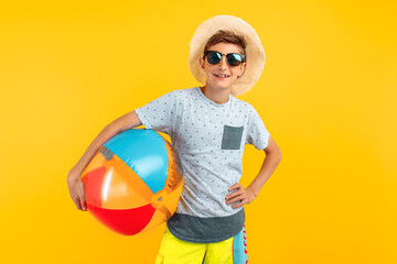 happy teen guy in a summer hat and sunglasses, with a sea ball on an yellow background