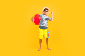 Fototapeta na wymiar Happy excited teen guy, stands with a beach ball and shows a winning gesture on a yellow background. The concept of summer vacation