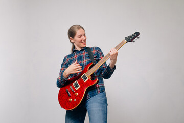 A young cheerful girl in jeans plays on red electronic guitar on bright background. Performing an energetic rock song