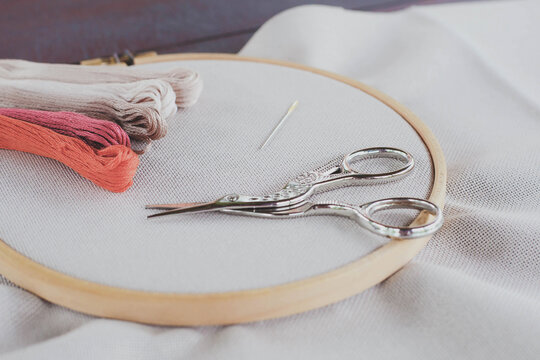 Canvas for embroidery with a cross embroidered in a round wooden hoop, multi-colored thread mouline thread, needle, scissors for needlework 