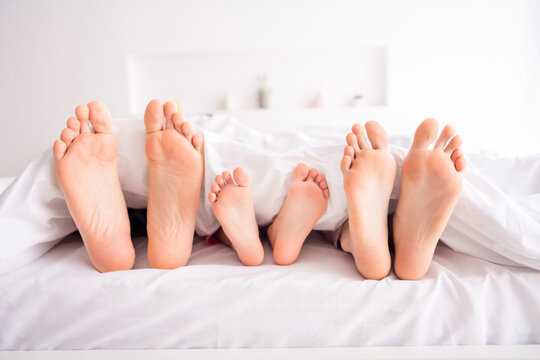 Closeup photo of happy family barefoot mommy daddy kid legs lying sheets sleeping early morning spend together quarantine weekend self isolation bedroom indoors