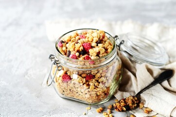 Homemade granola with berries and nuts in a glass jar on a gray background