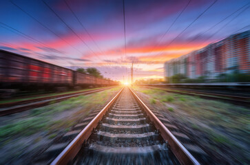 Fototapeta na wymiar Railroad and beautiful sky with clouds at sunset with motion blur effect in summer. Industrial landscape with freight train, railway station and blurred background. Railway platform in speed motion