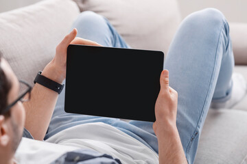 Surfing the internet. Man with smartwatch on couch at home and holds tablet with blank screen