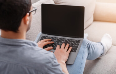 Fototapeta na wymiar Freelancer works from home. Guy typing on laptop, sitting on sofa