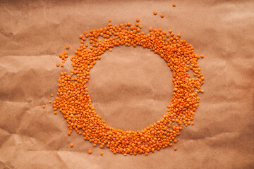 red lentils lie in the shape of a circle on a brown paper background. A place to design