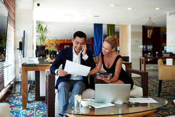 Successful smiling woman entrepreneur reveals documents his men colleague while work on digital tablet, cheerful intelligent business man look at working papers while having mobile phone conversation