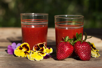 Strawberry juice with glass glasses on a wooden table and on the background of a green garden, on the table are ripe strawberries. Useful food, background, place for text.