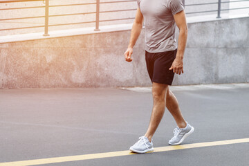 Fitness man athlete runner walking on the road. Person running working out living an active lifestyle training cardio in summer in sportswear and shoes. Lower body banner crop. Close up.