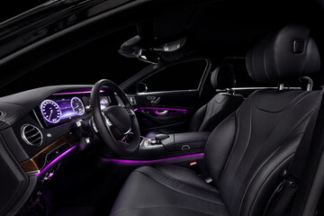 Fototapeta na wymiar Car interior from driver seat view. Black leather cockpit with violet ambient light.