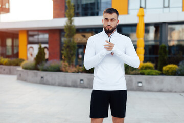 Cheerful male athlete resting after street workout session. Stylish urban young man in sportwear with a stylish hairstyle and beard stands near modern buildings in the city. Urban environment.