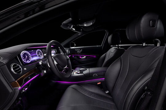 Car interior from driver seat view. Black leather cockpit with violet ambient light.