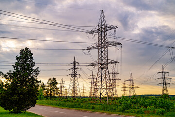 Electricity pylons bearing the power supply across a rural landscape during sunset. Selective focus.