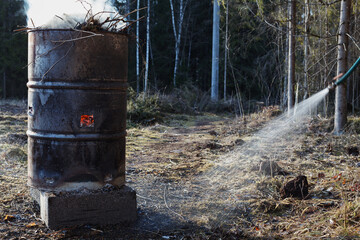 Water spraying from water hose near fire burning in old rusty barrel