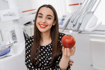 Beautiful girl holds an apple at dentist`s office. Red apple at girl`s hands.