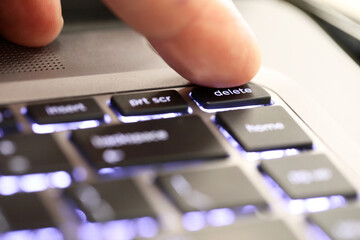 close up of a finger hitting pushing the delete symbol button tab on an illuminated laptop computer key board. The delete key © LincB