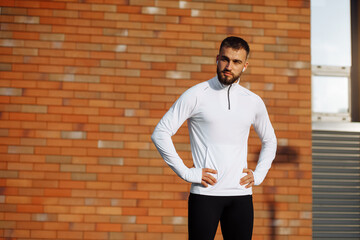 Fit young man in sportswear standing with his hands on his hips after a workout session or after running. Athletic man take a break after training.Fitness, sport and lifestyle concept. Brick wall.