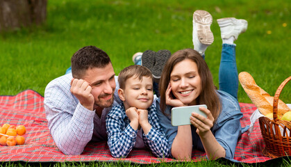 Happy family with smartphone watching entertainment video on picnic in park