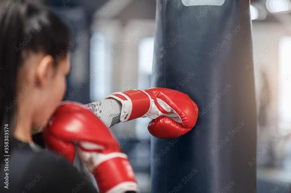 Wall mural Female boxer in gloves hitting big punching ball during self defence class at gym, empty space