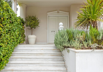 white marble stairs and door of an elegant family house entrance between vibrant green foliage