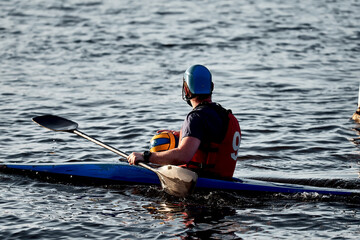 A guy wearing a canoe polo helmet rowing on a paddle and sailing on water with a ball in his hands....