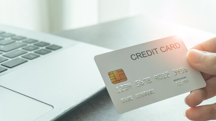 Woman hand holding a white credit card for shopping online or internet banking with laptop background and copy space. Online shopping concept.