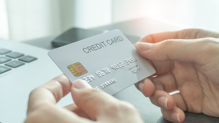 Woman hands holding a white credit card for shopping online or internet banking with laptop background near by smartphone. Online shopping concept.