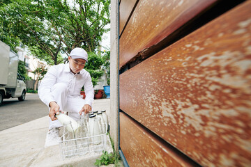 Asian milkman in white uniform delivering milk in morning and taking empty glass bottles, copy space