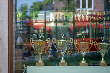 A street view at Trophy cups lined on a shelf throw the window of a shop.