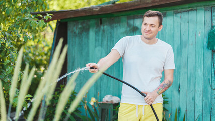 Man watering the garden from hose. Male spraying water on vegetables with a garden hose. A happy...