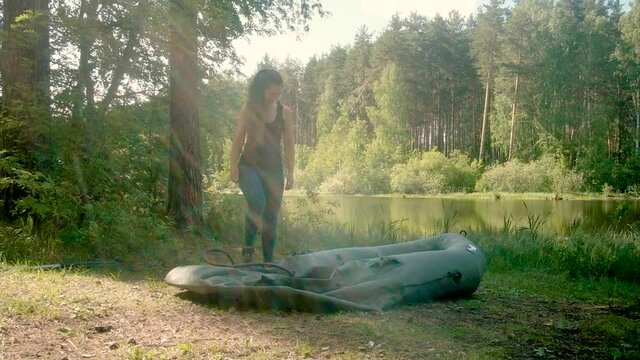 woman pumps an inflatable boat with a pump from the river bank. tent in the forest. Travel by water. concept of unity with nature. Active lifestyle. Recreation . Vacation Camping. Water alloy