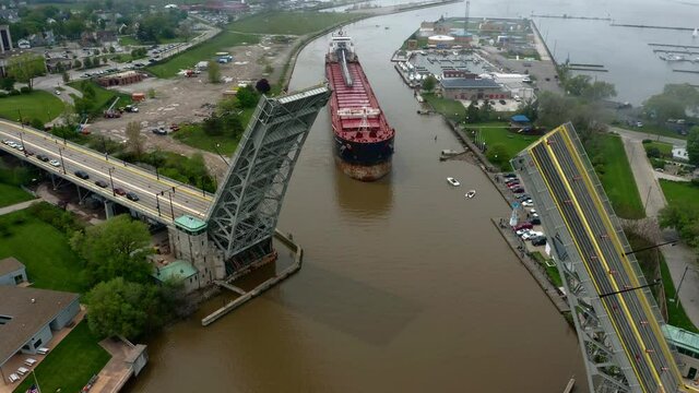 Aerial tracking shot of open lift bridge over the Black River in Lorain Ohio with cargo ship navigating to pass under