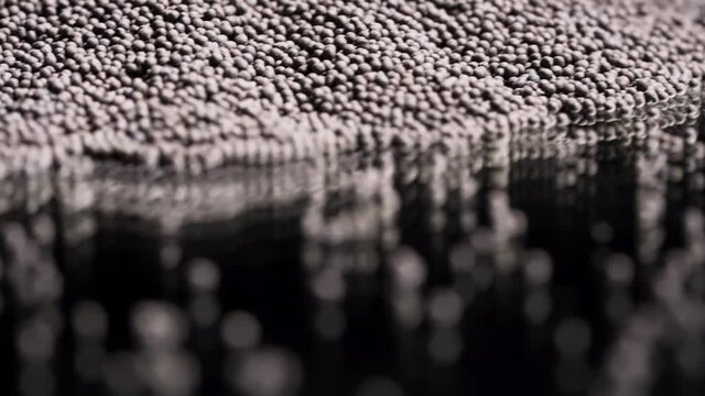 Close up of tiny gravel pile left on reflective black surface. Stock footage. Small stones at the laboratory during quality control of contruction materials process.