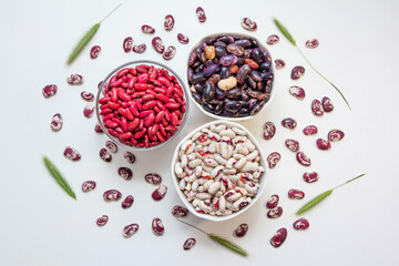 Colorful dried raw beans in bowls and on white table surface