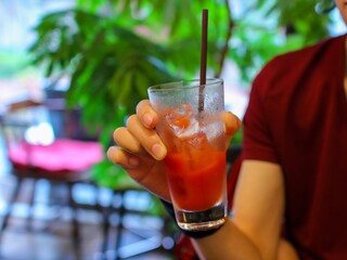A glass of tomato juice held by a male hand in a restaurant