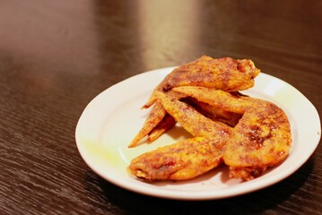Japanese food, fried chicken wings (tebasaki) on a small white plate on a black table. They are seasoned with hot spices. 