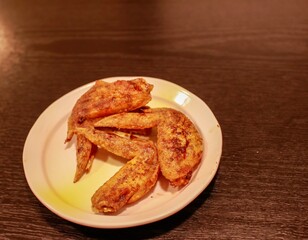 Japanese food, fried chicken wings (tebasaki) on a small white plate on a black table. They are seasoned with hot spices. 