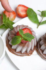 Chocolate fudge garnished with half a strawberry with petals. Garnished with sprigs of mint and strawberries. On the white surface of the table.