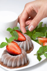 Chocolate fudge garnished with half a strawberry with petals. Woman decorates dessert with mint and...
