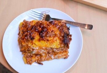 A slice of beef Lasagna on a white plate with a fork on a table from the top