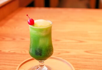 Matcha float drink (cold matcha drink with vanilla ice on top) on a wooden plate on a wooden table with a cherry