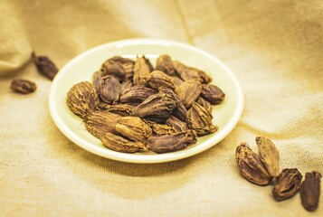 Cardamom seeds on a small plate on a beige fabric background. Cardamom is used as flavouring and cooking spice in both food and drink, and as a medicine.