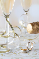 A close up of wedding bands with champagne flutes and gold ribbon in behind.